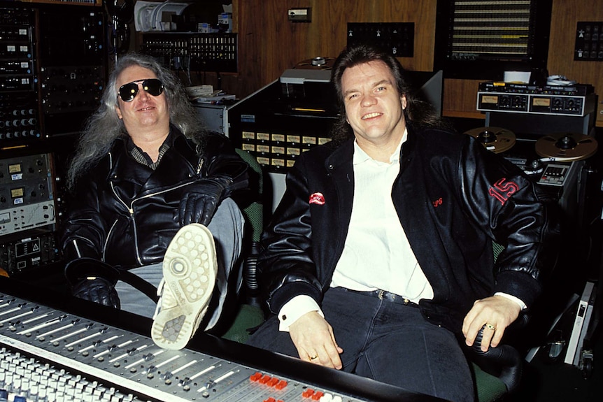 Two men sitting in a recording studio smiling for the camera.