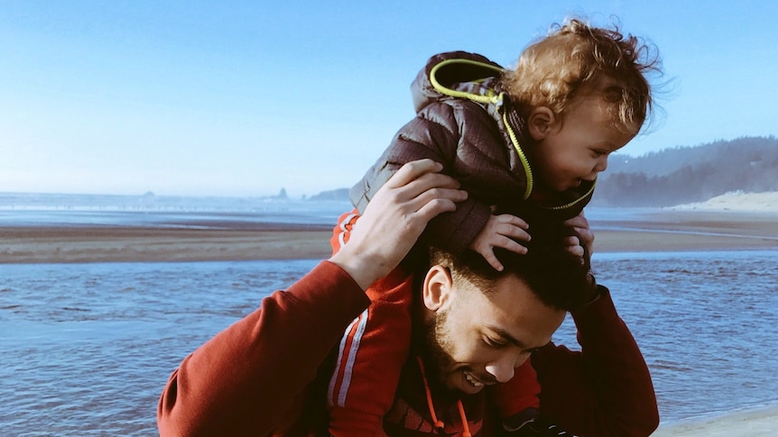 A man holding his child above his head at a beach.