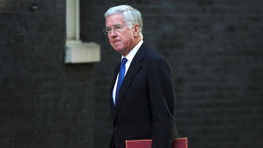 Michael Fallon walks along the street holding a red folder.