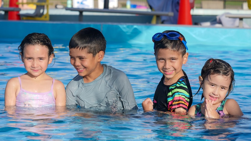 Four young children looking happy in a public swimming pool.