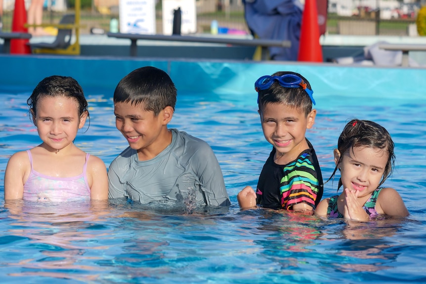 Four young children looking happy in a public swimming pool.