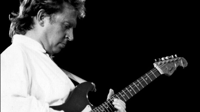 Andy Summers plays the guitar on stage, the photo is in black and white