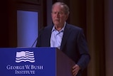George W Bush stands behind a lectern. 