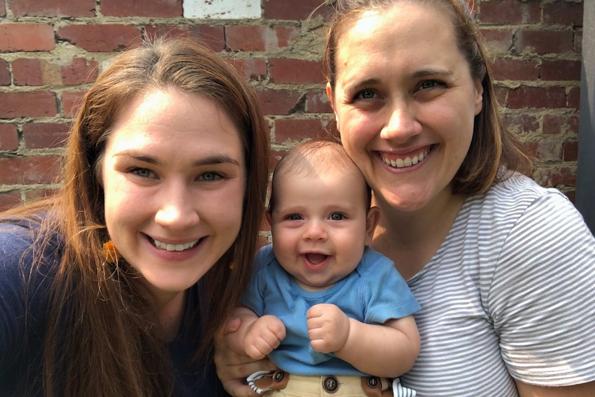 Two women smile for a camera while holding their baby boy, who was born using donor sperm.