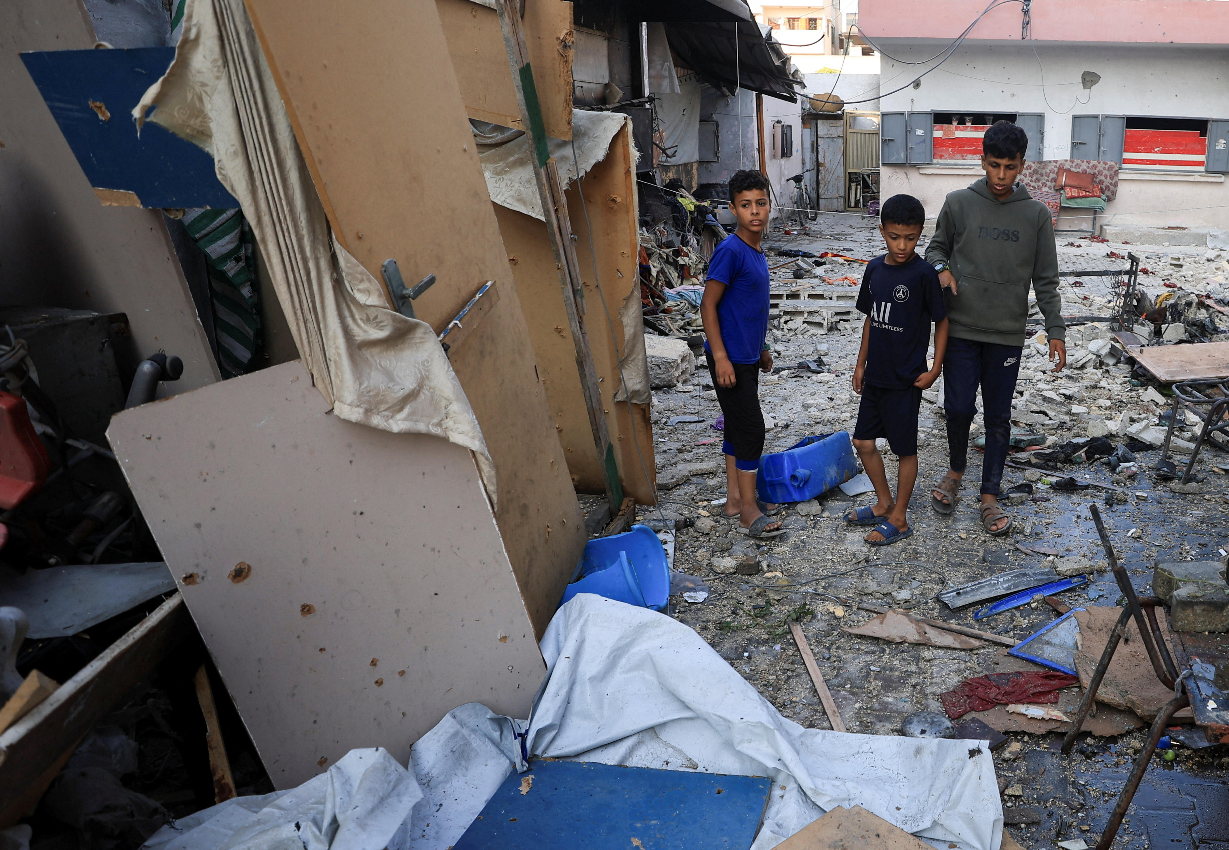 Three Palestinian boys looking through the remnants of a bombed out classroom.