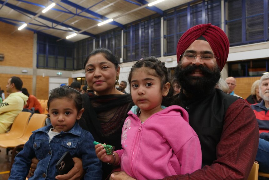 A sikh man with daughter sitting on his lap and wife and son next to him