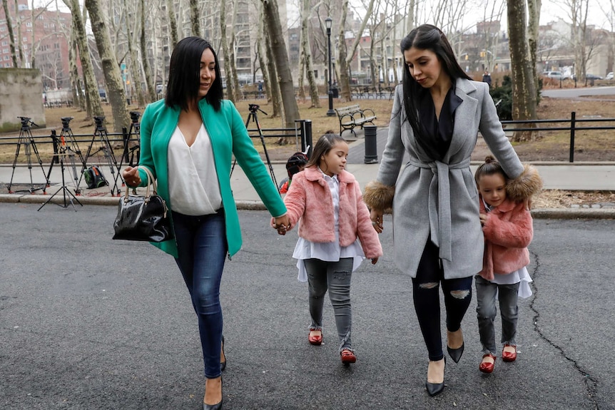 Emma Coronel walks across the street with a woman and children.