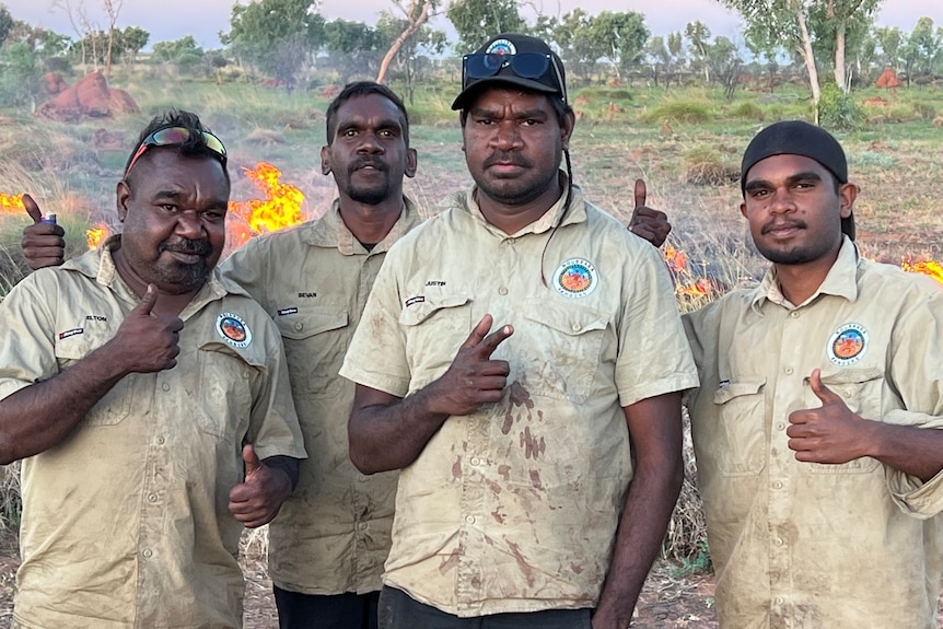 A group of men stand in front of burning grass.