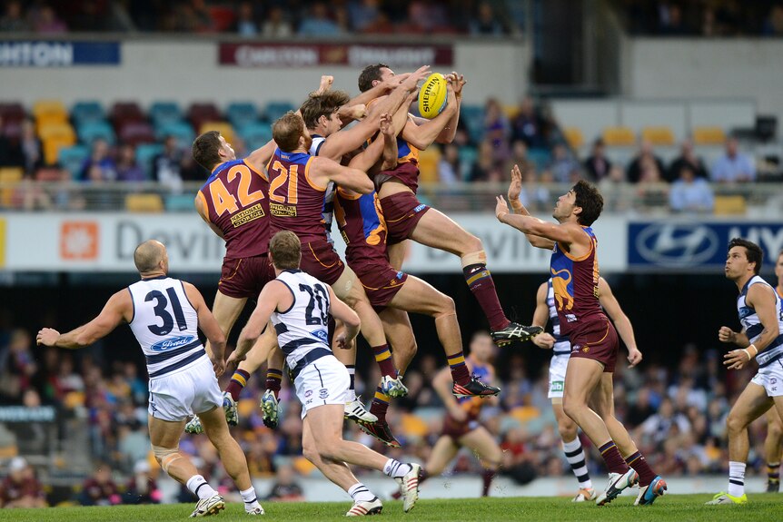 A tall ruckman for the Brisbane Lions reaches out and grabs the ball high in the air, with a sea of arms and players behind him.