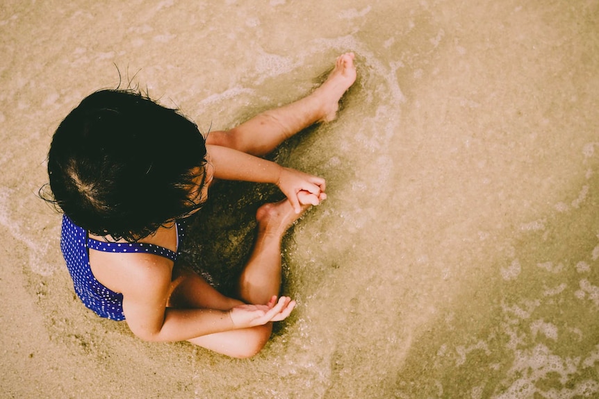 A little girl sits at the beach