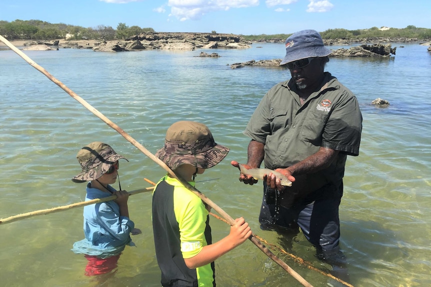 Will and Brodie Pittman hold fishing spears they made while Bundy, a local Bardi man, shows them a fish he speared.