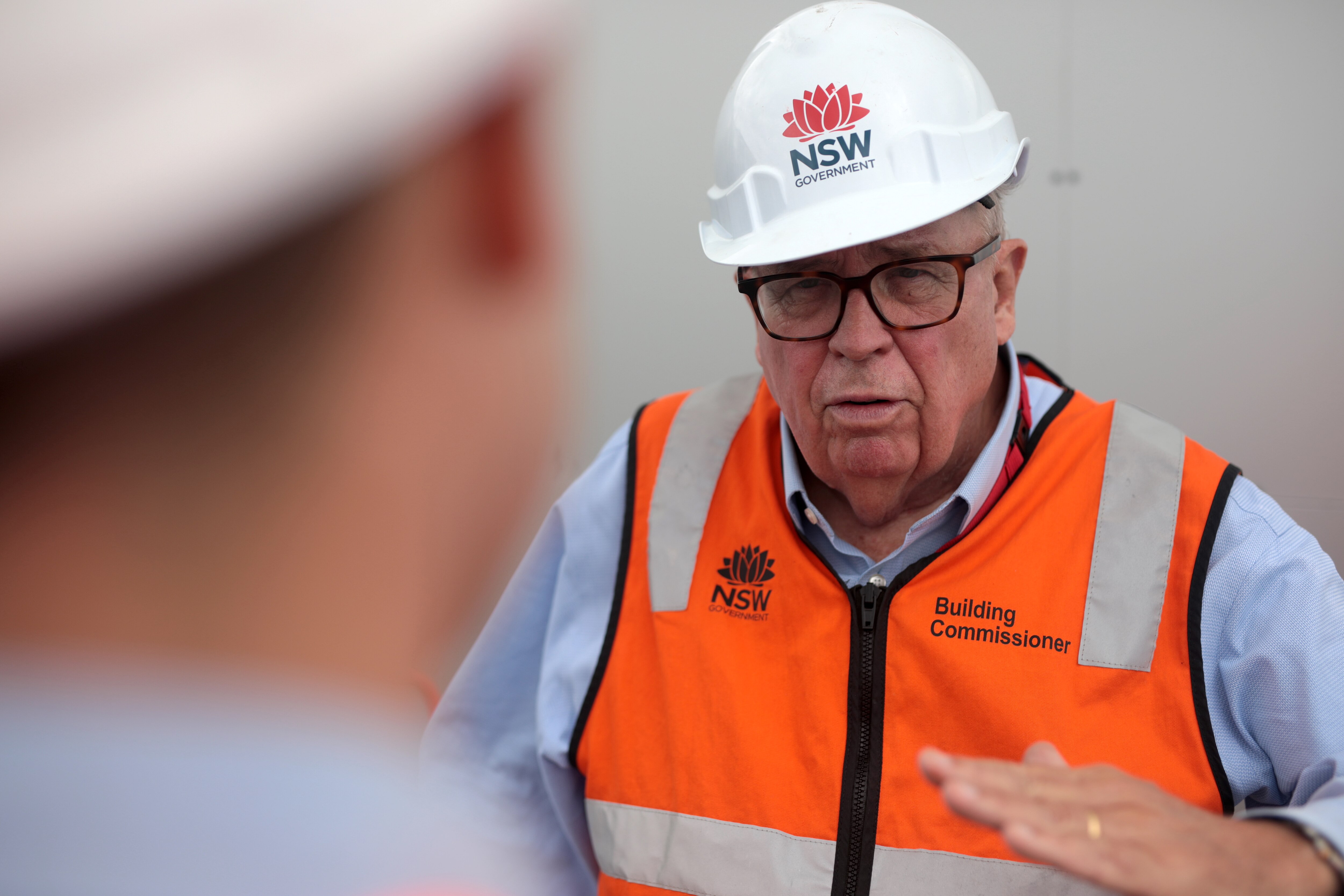 Man in orange hi-vis and hard hat having a conversation with a reporter.