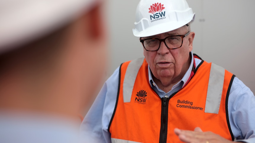 A man in high-vis and a hard hat having a conversation with a reporter.