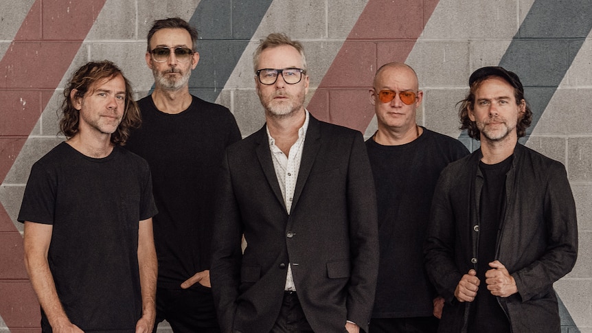 The five members of The National pose for a photo outside a striped brick wall