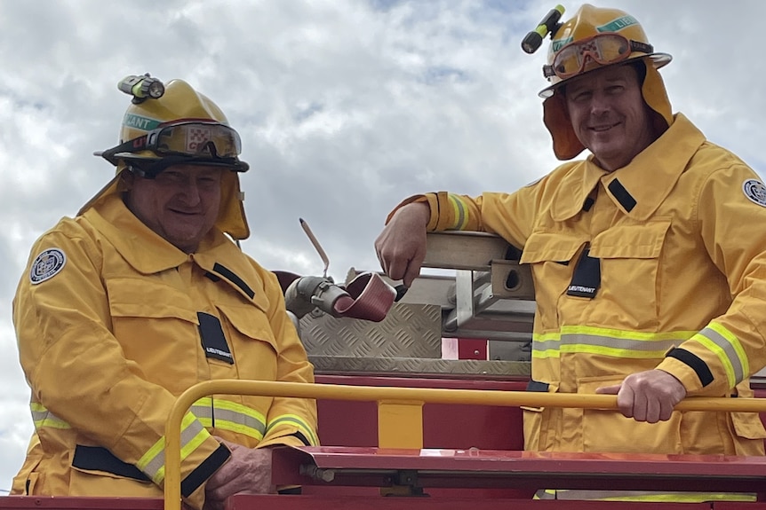 Two CFA volunteers stand up on their truck in their fire fighting kit