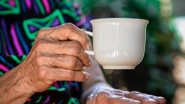 A close-up of a senior's hand holding a mug.