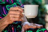 A close-up of a senior's hand holding a mug.