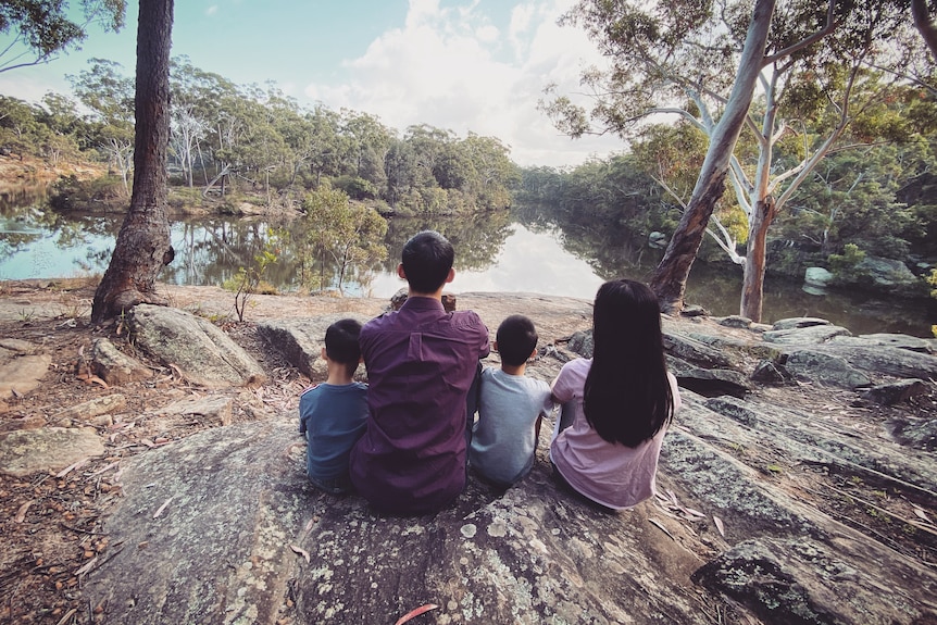 Award-winning maths teacher Eddie Woo sitting on a rock overlooking a river with his wife and children.