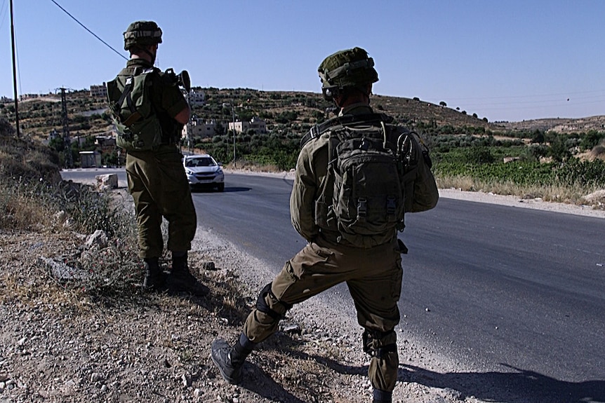 Israeli soldiers at a pop-up checkpoint watch cars driving along a road near Beni Neiem village.
