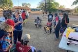 Community members and nurses stand around on the footy oval in Ngukurr