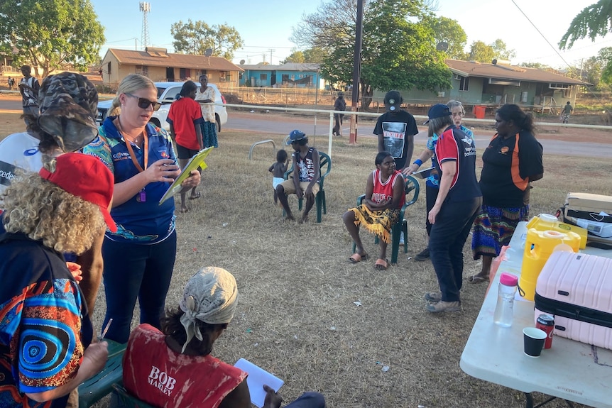 Community members and nurses stand around on the footy oval in Ngukurr