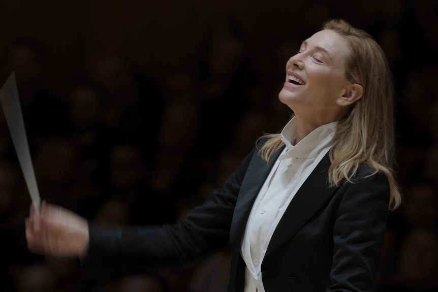 A brown-haired, 50-something woman smiles broadly, her eyes closed, as she moves a baton through the air