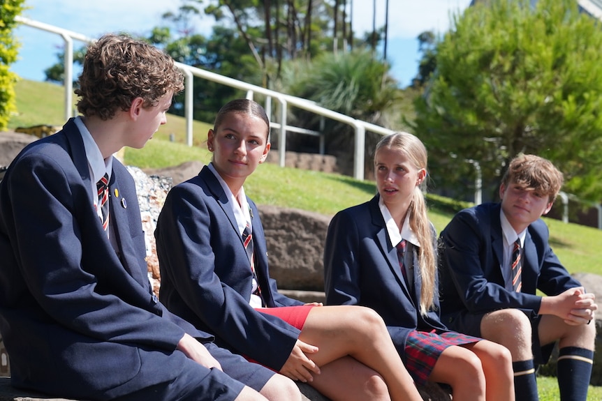 Students in private school uniforms with jackets sitting outside in the sunshine.