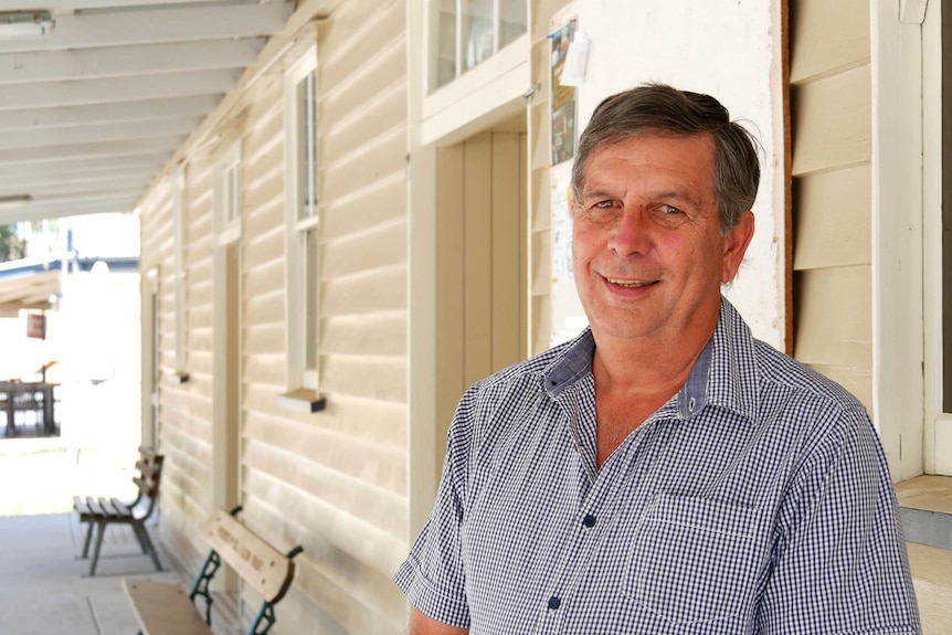 A man stands smiling outside a timber building with park benches.