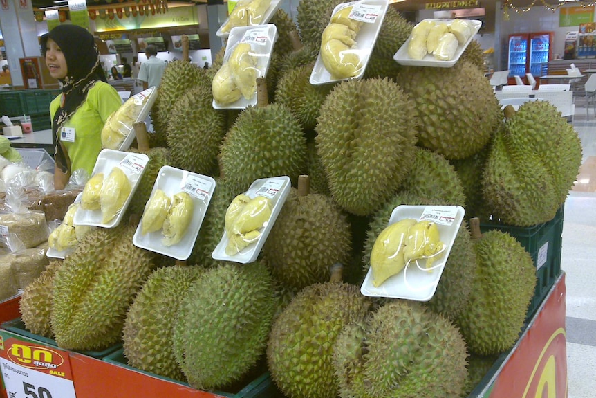 A woman is standing next to a cart of durians.