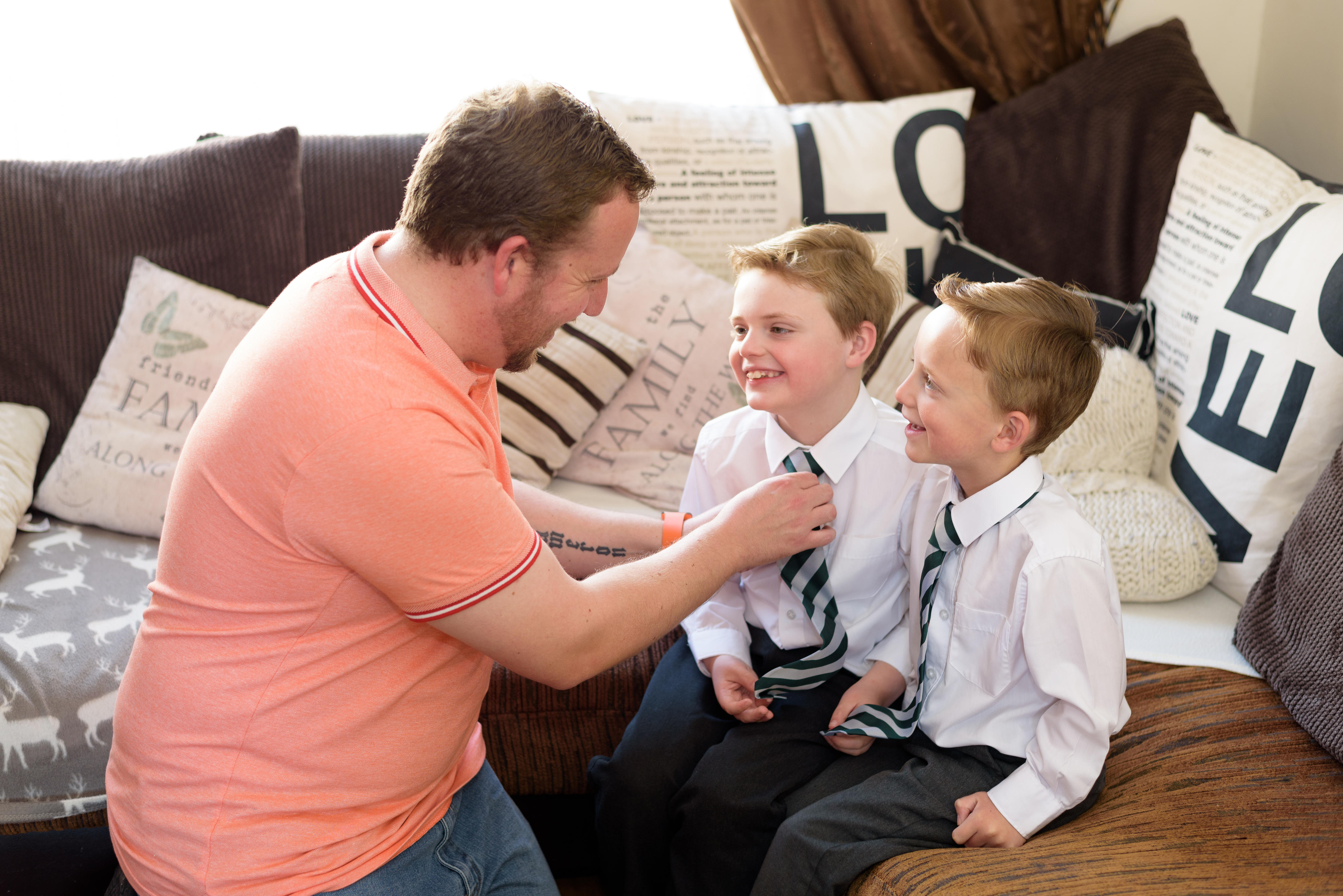 Dad kneeling down next to two boys in uniform sitting on the couch.