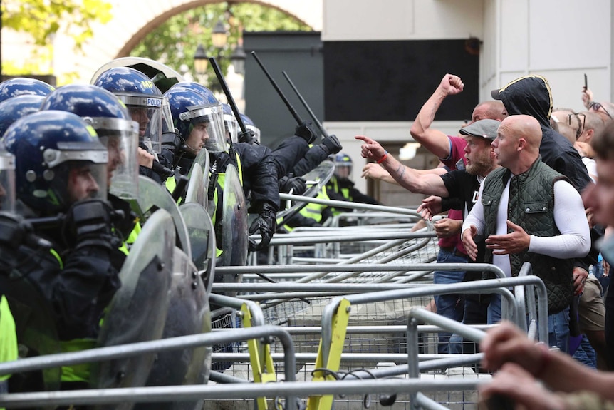 Police are confronted by protesters as they stand behind metal barricades.