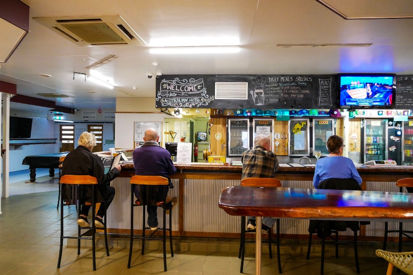 Four older people sit at a bar at an outback pub. 