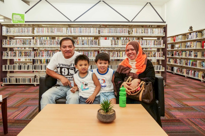 A family of four sit at a couch in a library, smiling.