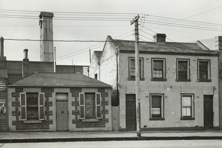 A black and white photo shows a single storey and double storey Victorian terrace side by side.