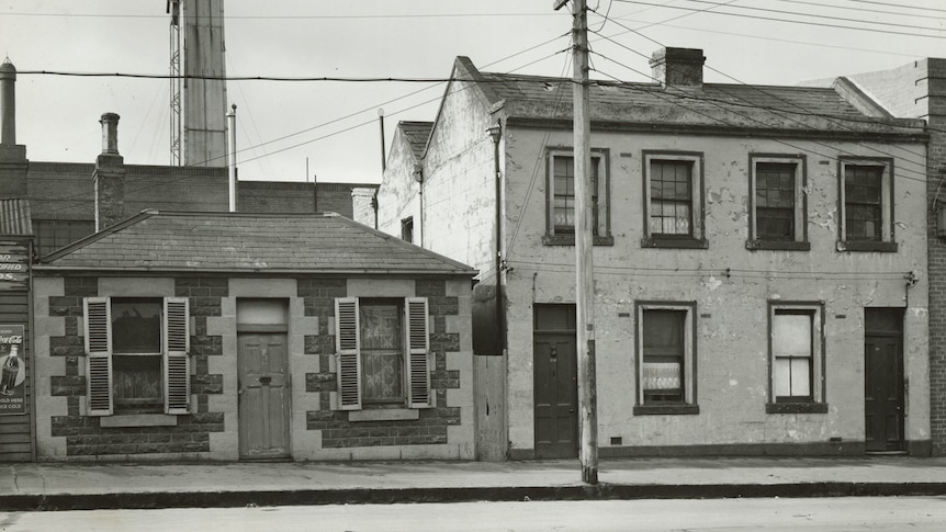 A black and white photo shows a single storey and double storey Victorian terrace side by side.