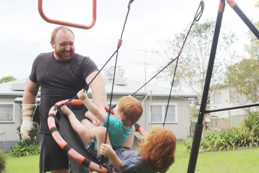 A man playing with his two kids on a swing outside their home