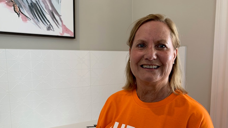 Woman stands smiling in an orange shirt