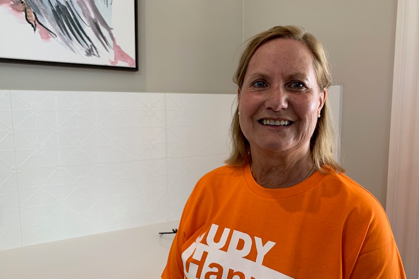 Woman stands smiling in an orange shirt