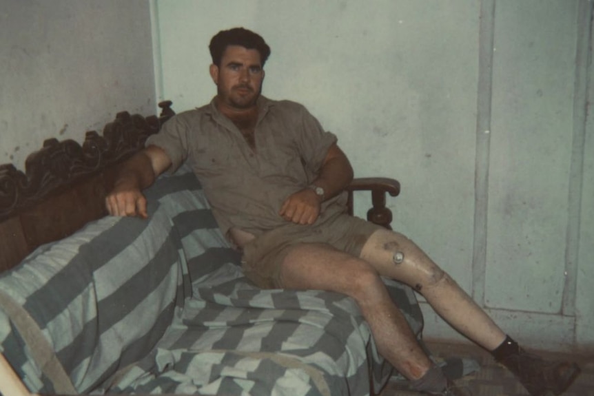A young man with dark hair and a prosthetic leg sits on a sofa.