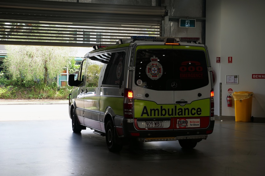 The back of an ambulance vehicle with illuminated break lights. A garage door is opening in front of the van. 