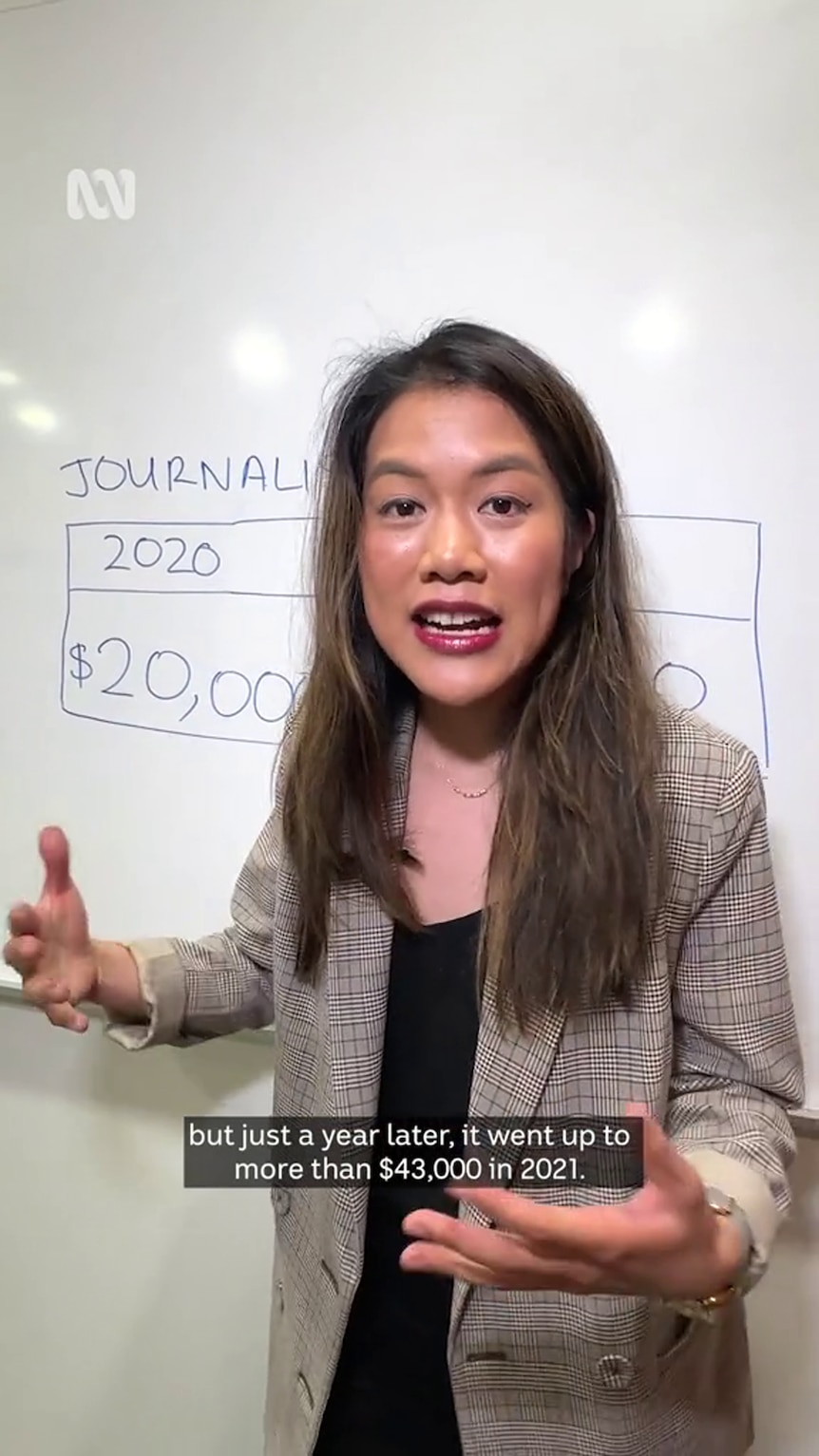A young Asian woman gestures with her open hands standing in front of a whiteboard