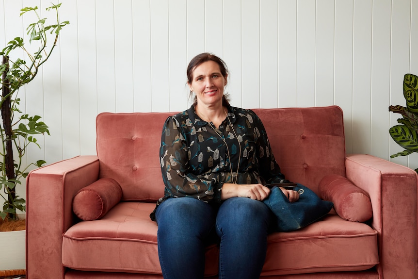 A middle-aged woman sits on a couch, holding a handbag