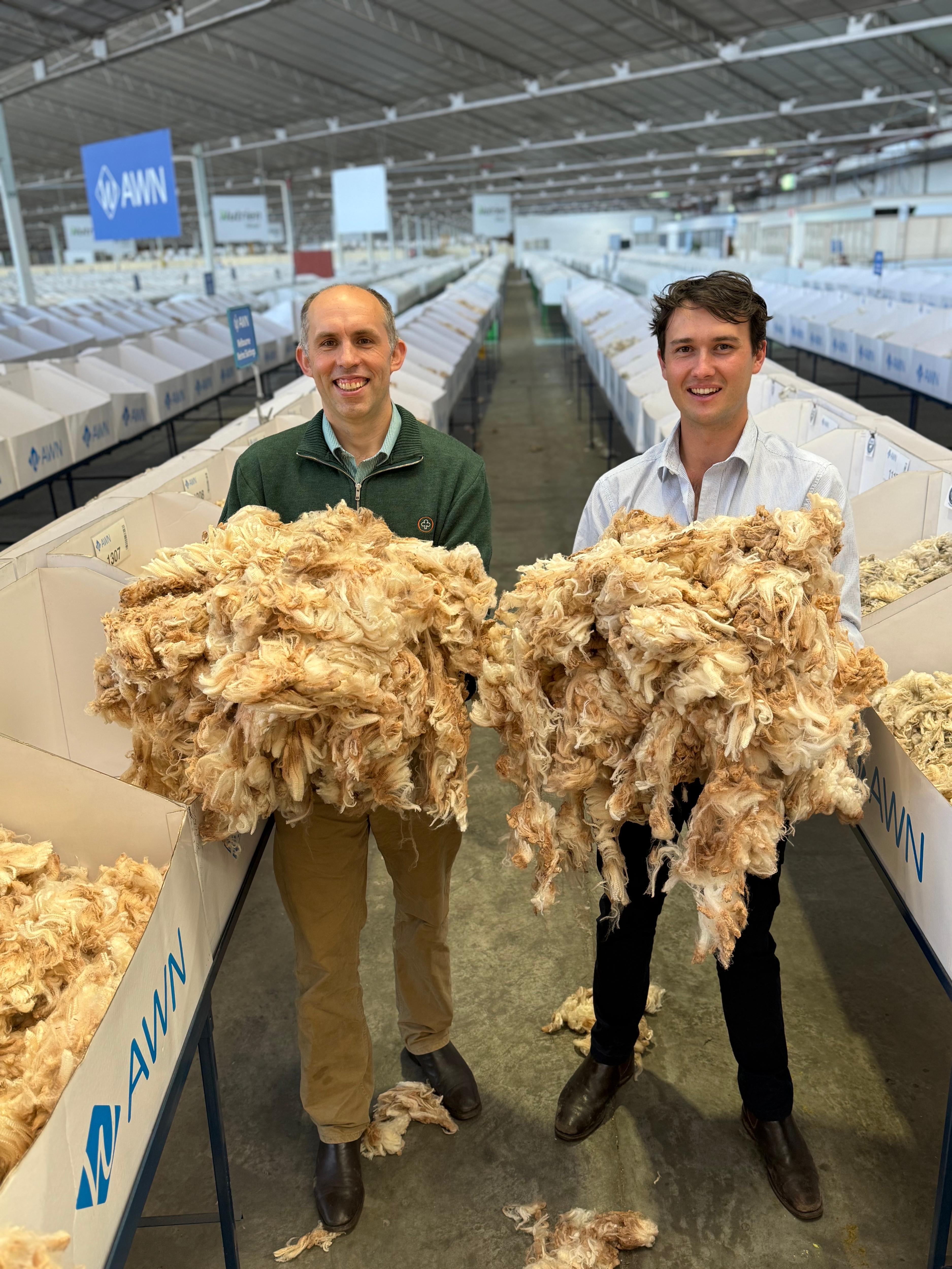 Two men stand holding sheep's wool in their hands.