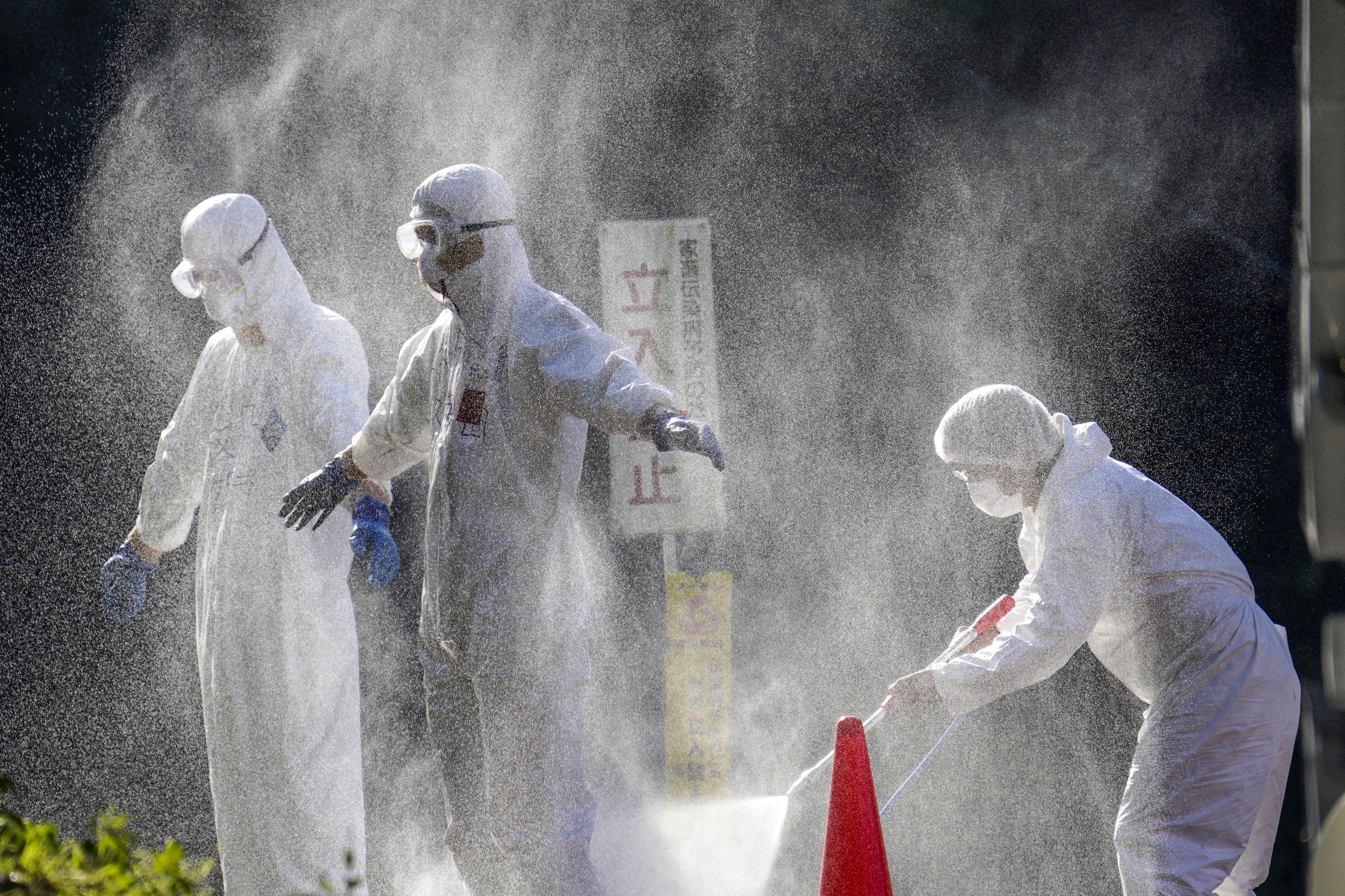 A person wearing PPE is sprayed down. 