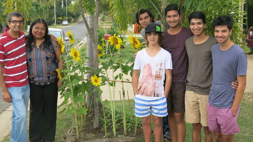 garden owners and young people stand around a clump of sunflowers growing on the footpath