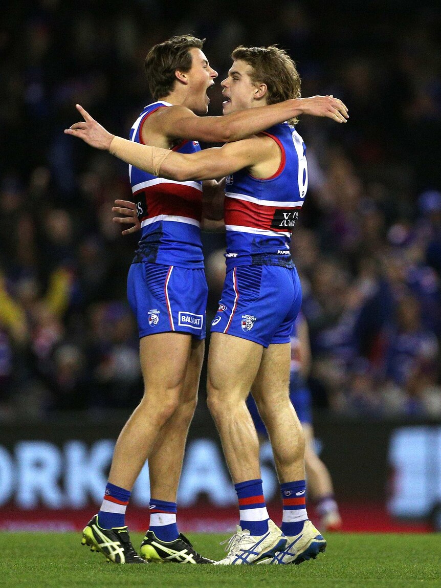 Two male AFL players stand and hug each other as they celebrate a goal for their team.