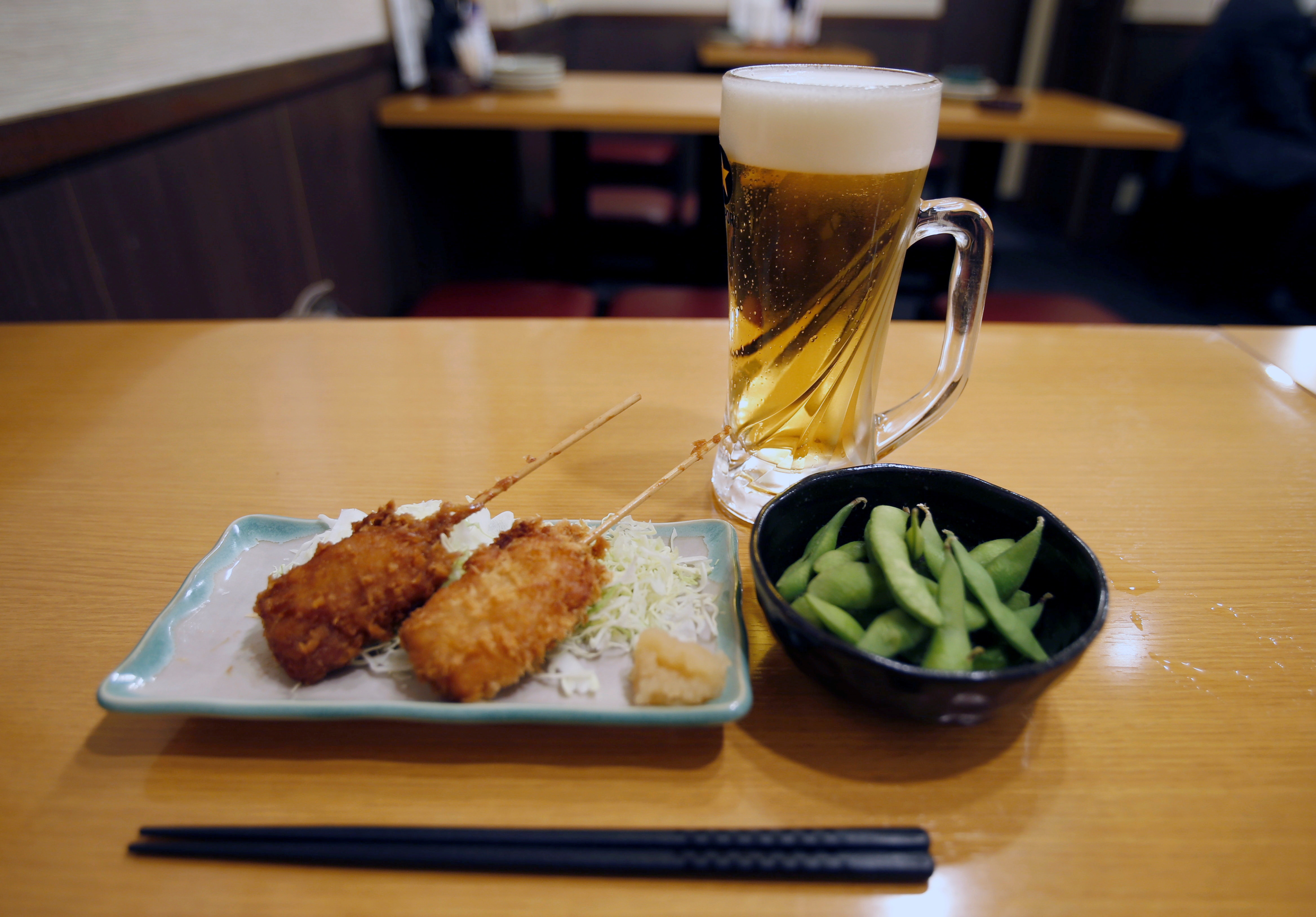 Brochetas fritas, soja verde y un vaso de cerveza en un restaurante de Japón