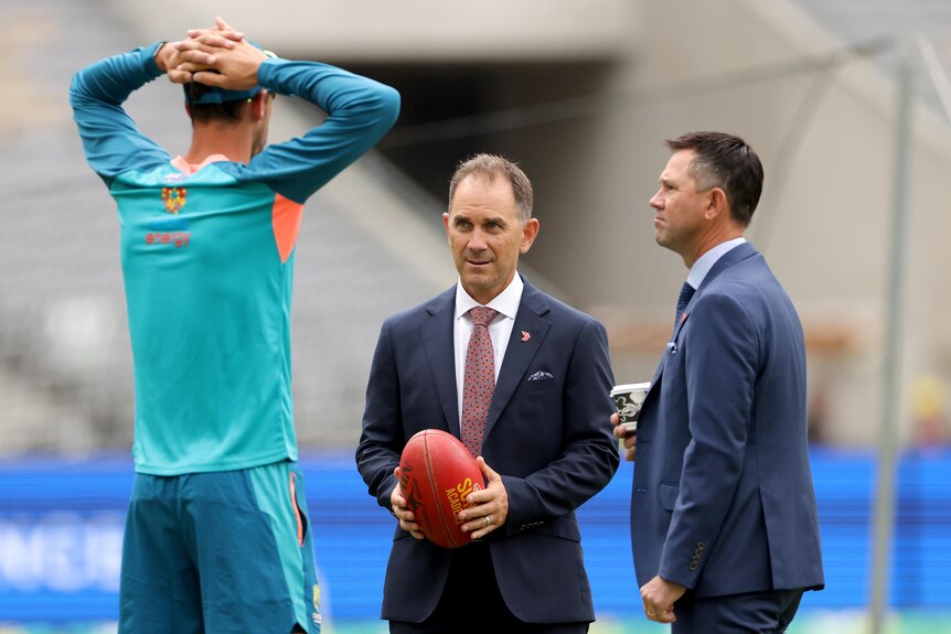 Mitchell Star stands with his hands on his head as he speaks to Justin Langer and Ricky Ponting who are in suits