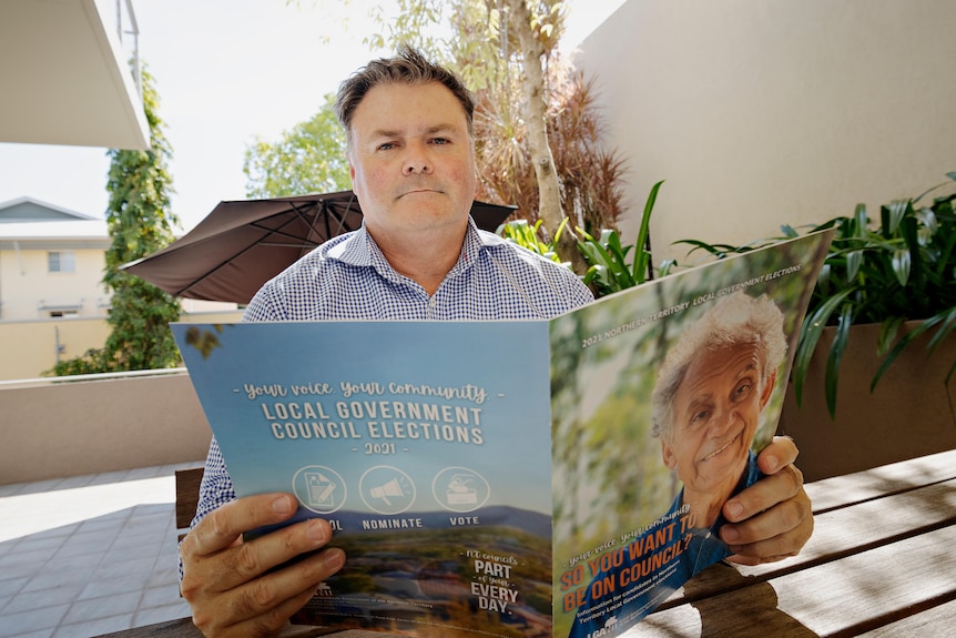 Local Government Association of the Northern Territory CEO Sean Holden sits at a table reading a election pamphlet. 