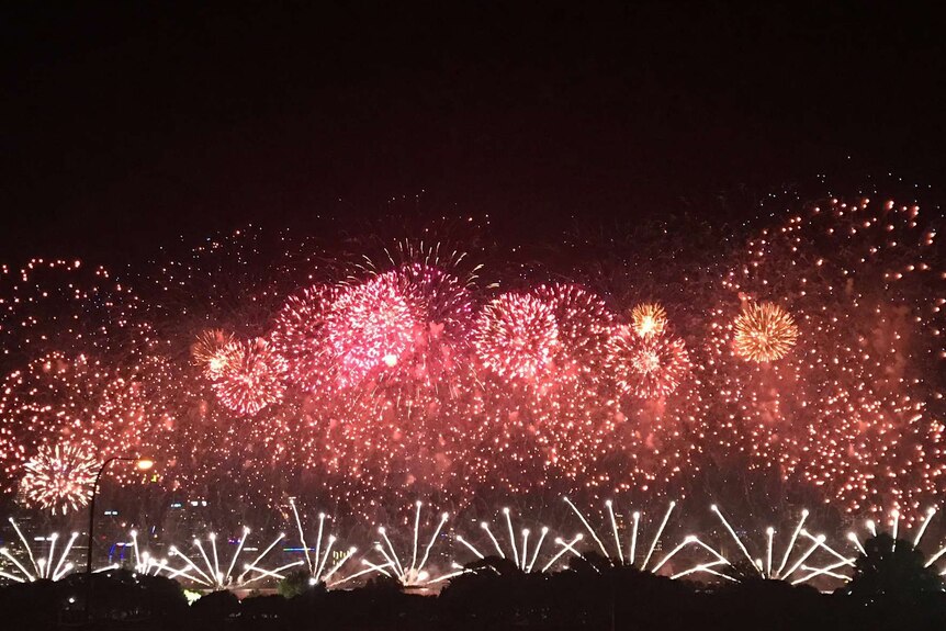 Red and orange fireworks light up a dark sky over the Swan River in Perth.